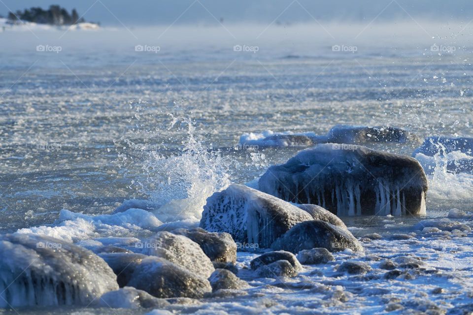 Ice covered rock by the Baltic Sea that is about to freeze over with water splashing against the rocks in Helsinki, Finland on 14 January 2021.