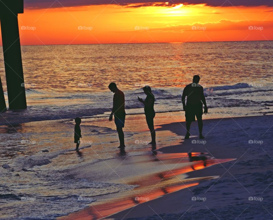 Blazing sunset on the Gulf of Mexico at low tide. A family is silhouetted on the sandy beach as the waves roll in