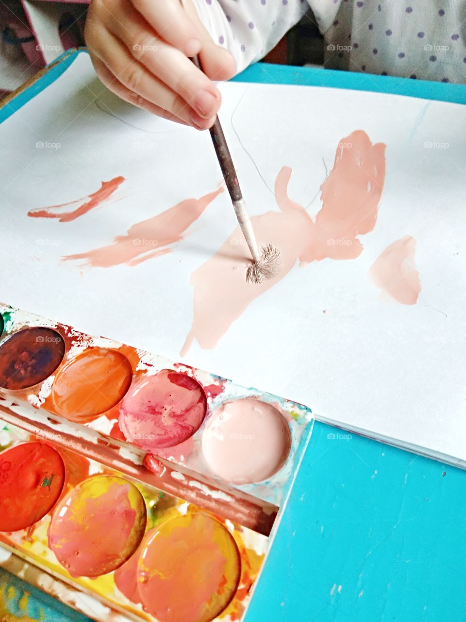 child's hand holds the brush and paints in the album with watercolors