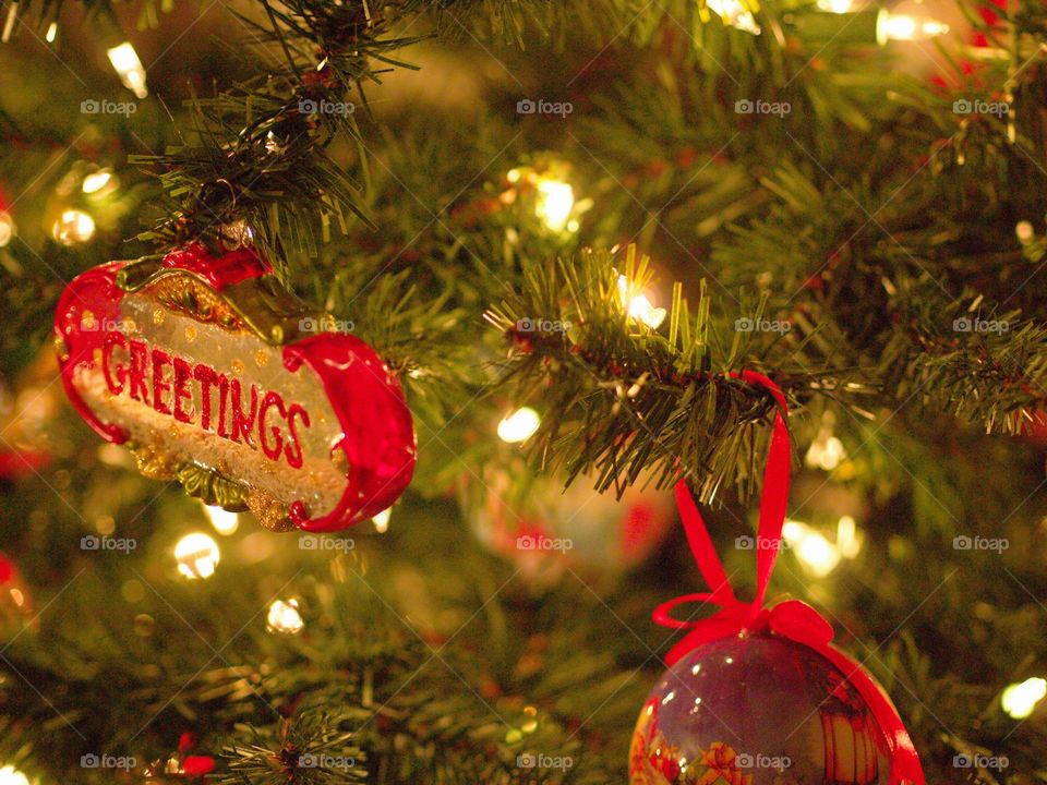 A pair of ornaments hanging from a Christmas tree with softly glowing lights. 