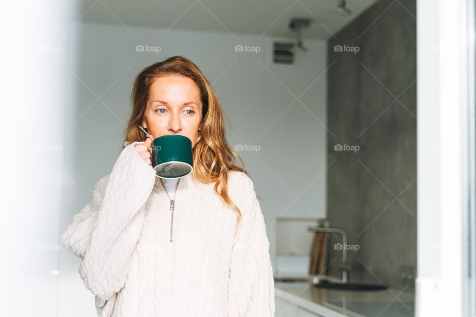 Beautiful woman with cup of hot drink in kitchen at home in winter 