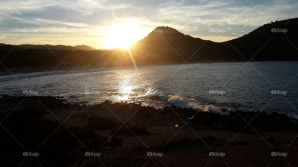 a beautiful sunset / sunrise on a warm summer evening on the holiday island Mallorca. You see the beach and the sea, which are surrounded by the mountains.