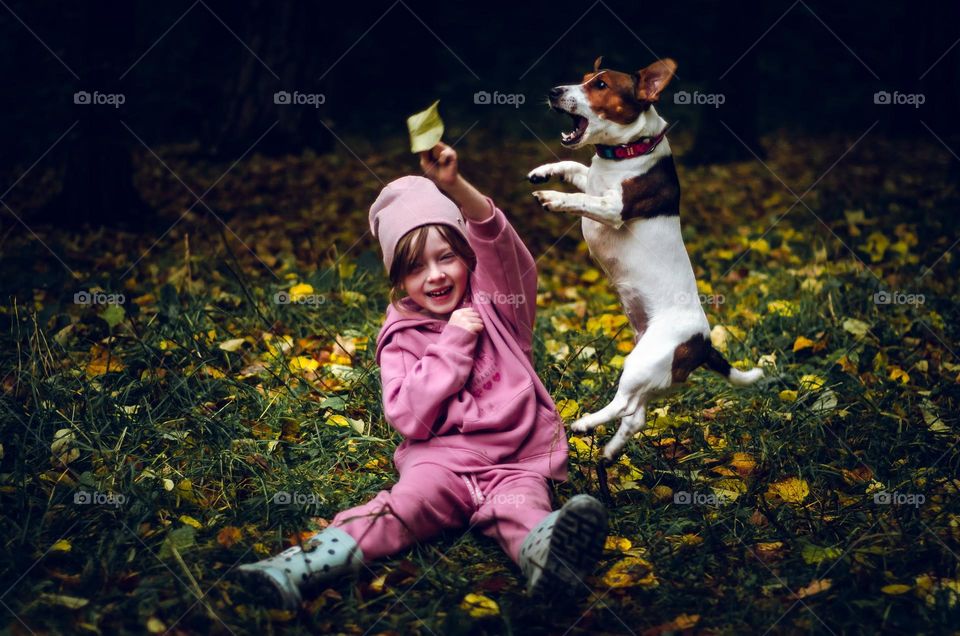 A little girl plays with her dog in the autumn forest.