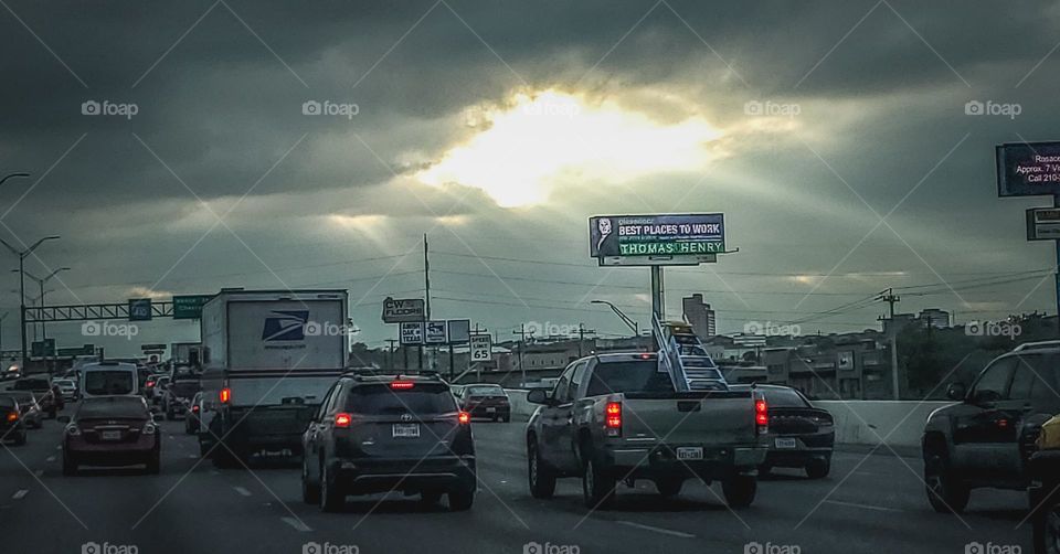 Commuting in traffic at sunset as storms set in with glimpse of sunlight peering through the clouds.