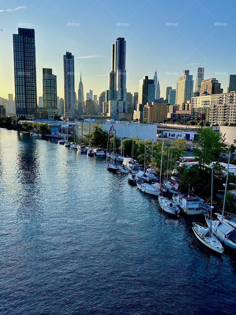 This is the view from the “Pulaski Bridge” that connects “Greenpoint”, Bklyn to LIC onto “Newtown Creek”, ocean inlet of the “E River”. Many lovely boats are lined up here side by side. In the distance we see “Manhattan”. 2024. Hypnotic Productions