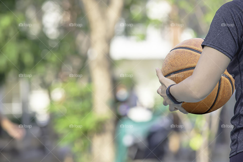 Leather basketball in hand of a woman wearing a watch Background blur tree in park.