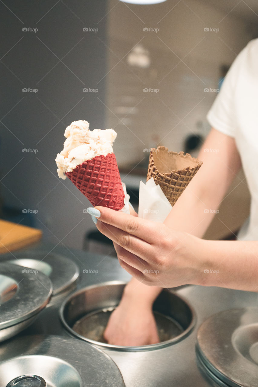 Seller selling couple scoops of  ice cream in a candy shop by a street. Woman putting a scoops of ice cream to a cones