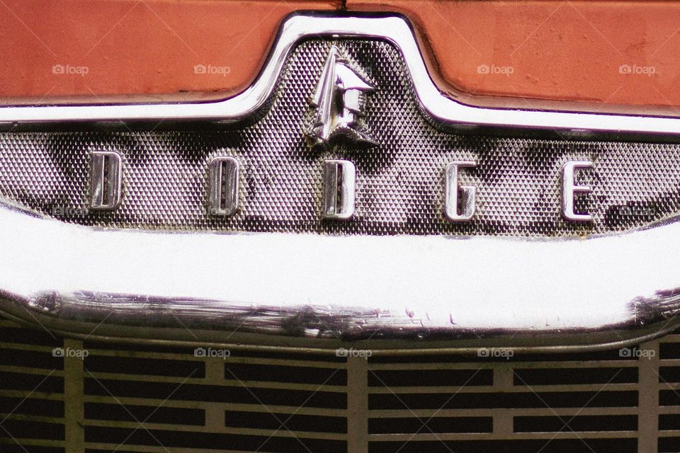 A closeup of the chrome grill of a red vintage Dodge car. 