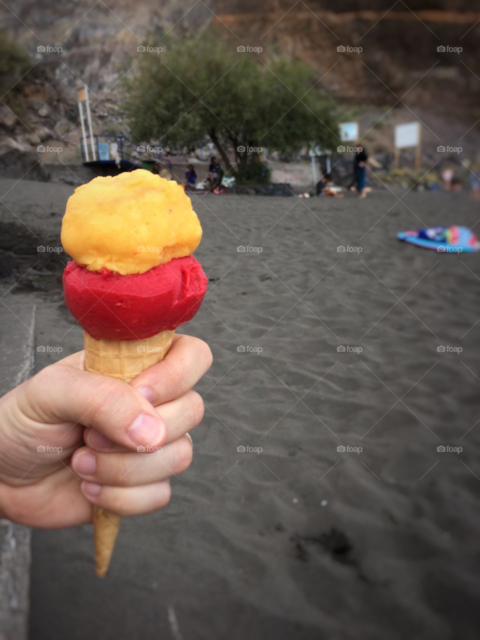 Hands holding ice cream cone - with view to the dark Sand Beach on La Gomera