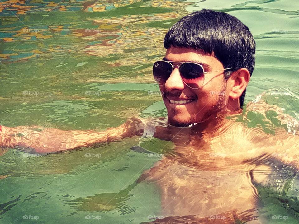 sunrays falls on colourless water and makes the photo energetic . there is a boy playing in swimming pool on a sunny day
