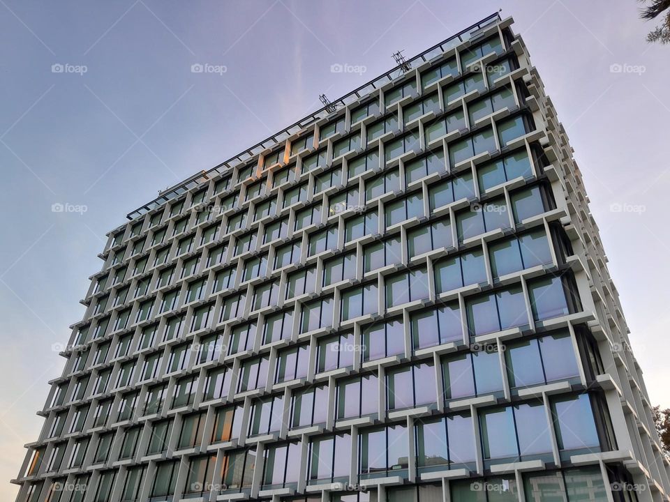 a tall building, rainbows reflected in its glass, purples, violets,  yellows and greens