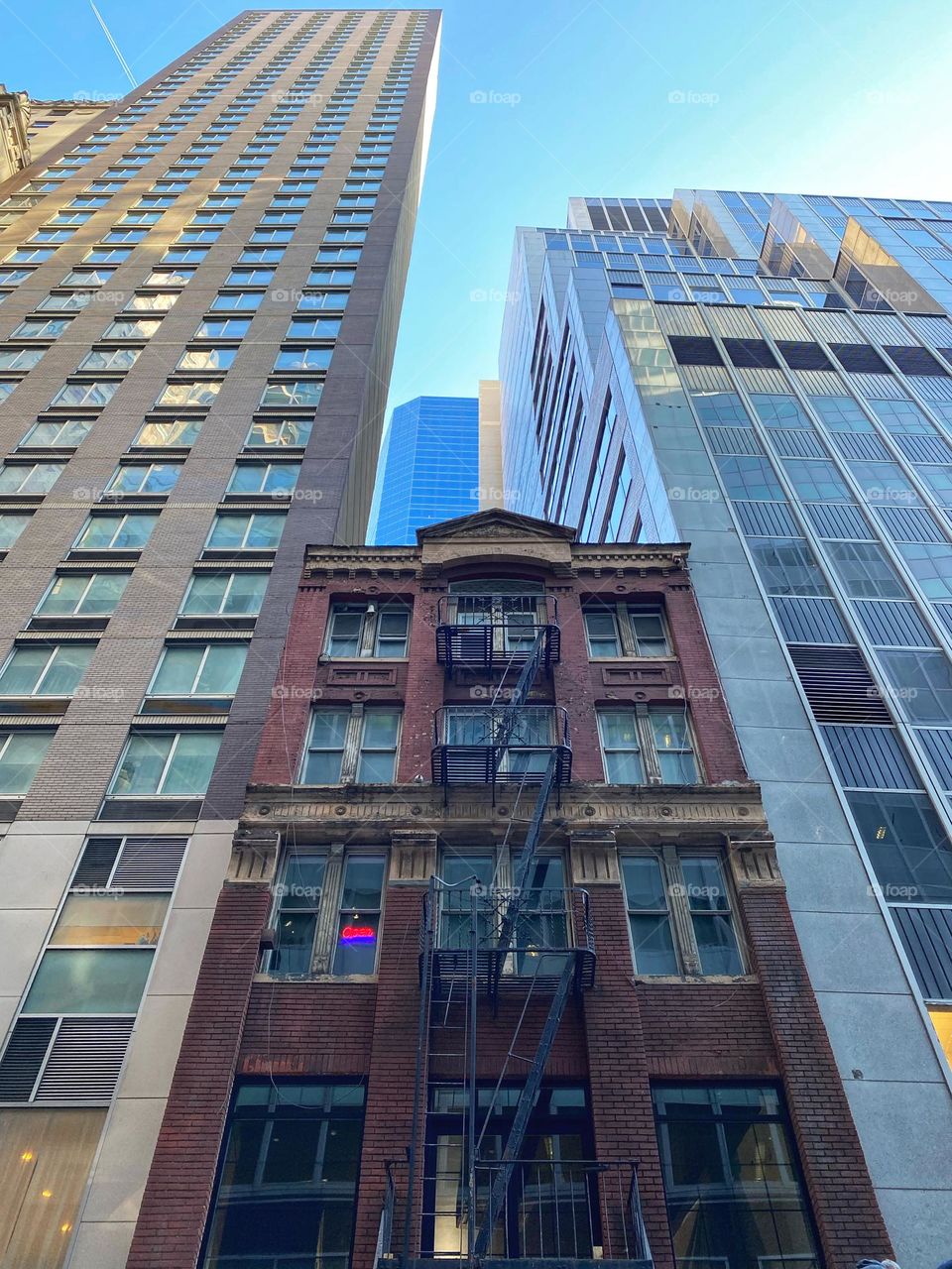An old building sandwiched between modern skyscrapers