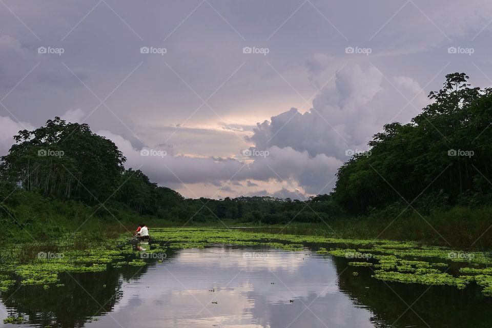 Piranha fishing on amazon river. Sunset through stormy cloudy skies. Two fisherman, near Iquitos Peru.