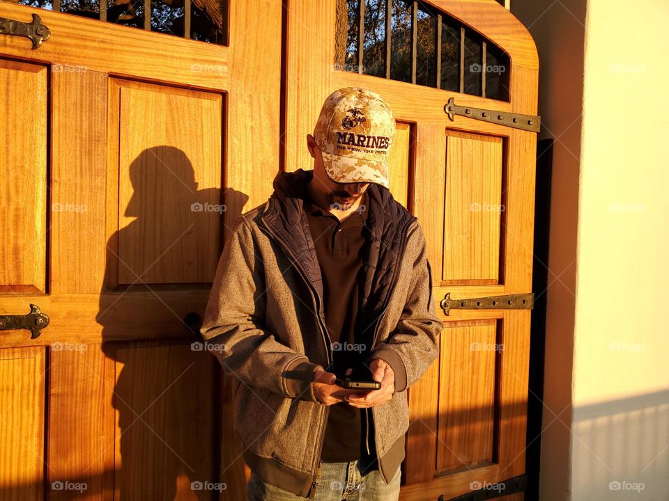 A man standing in front of beautiful solid wood Spanish style courtyard double doors at sunset.