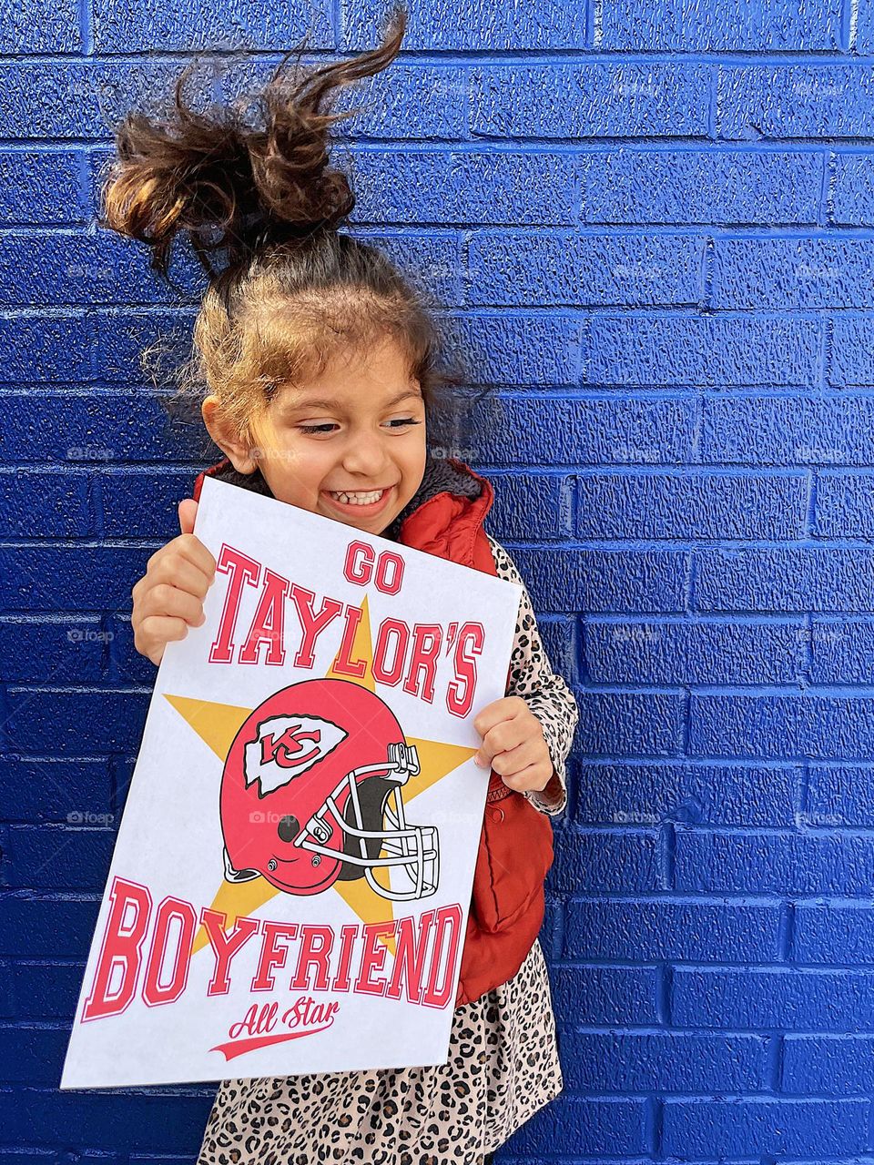 Toddler girl cheers for football team, toddler holds Taylor’s Boyfriend sign, cute toddler cheers for Kansas City Chiefs, cheering for a football team, toddlers that love football 