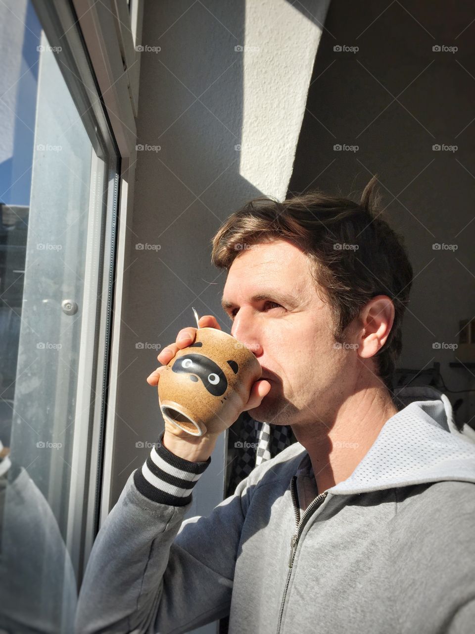 Man at window with cup of of coffee . Young Caucasian man in casual drinking hot coffee next to window
