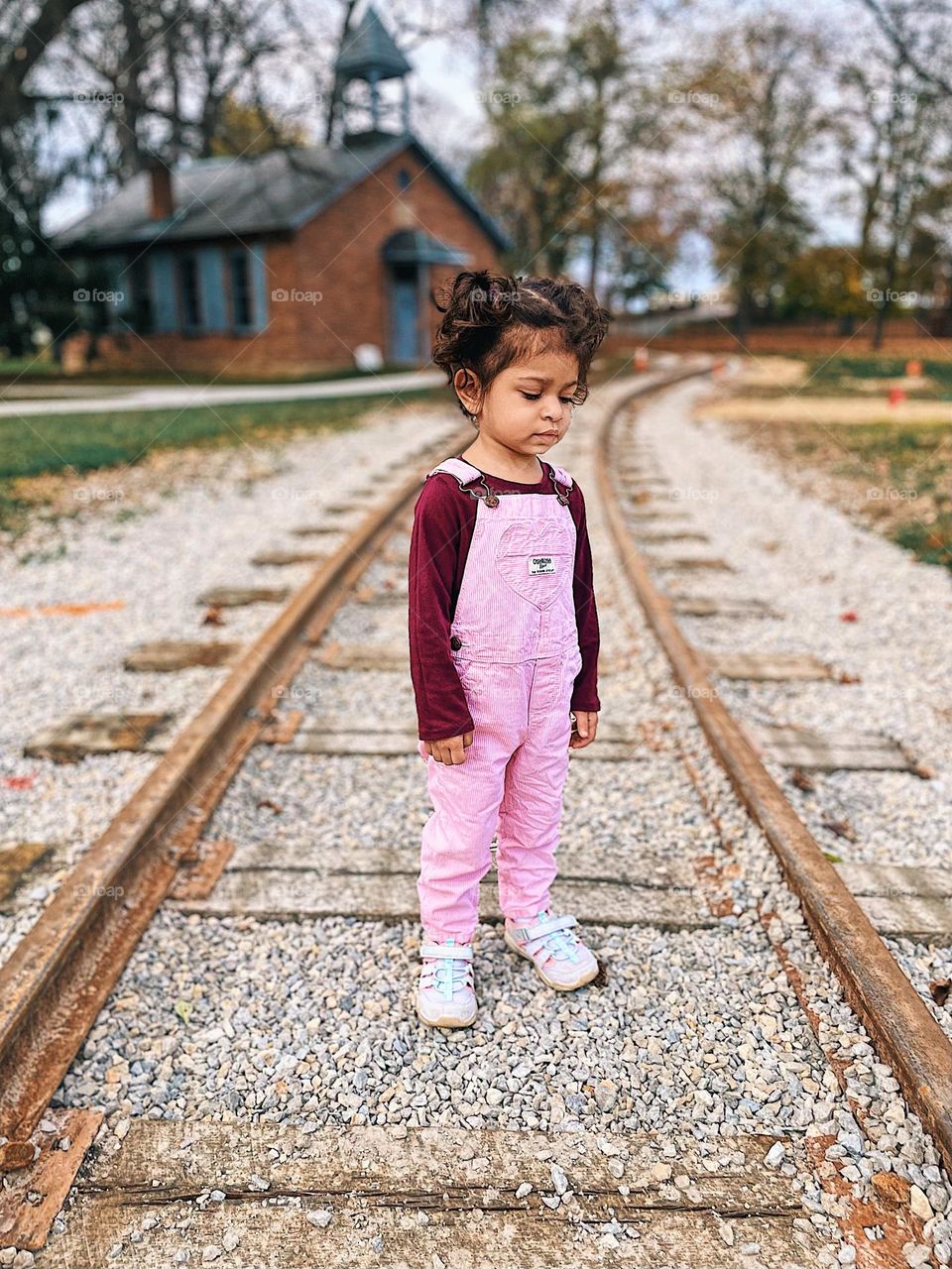 Sad child wearing overalls on a train track, toddler walking on train tracks expressing sadness, facial expressions of toddlers, sadness on the face of a toddler, toddler showing emotion, toddler girl is portraying sadness on her face, toddler is sad