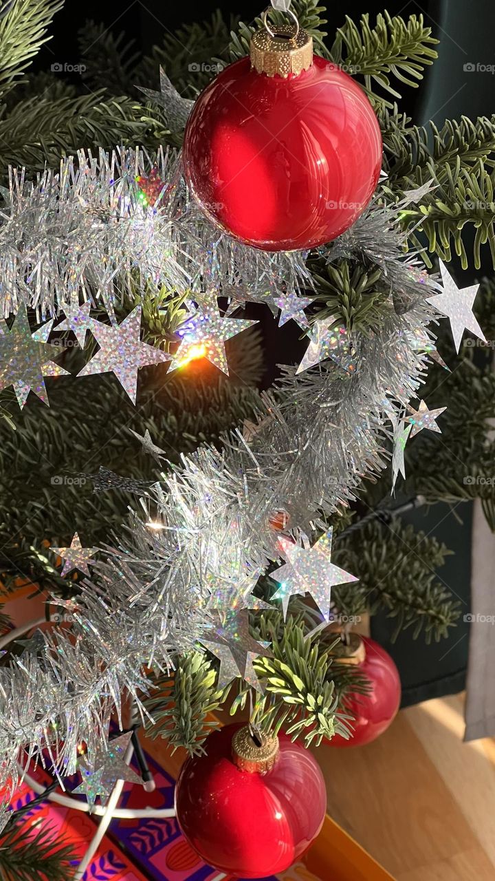 Red Ornament in the Sunlight
A sparkling red ornament catches the sun, glowing among shimmering tinsel on the Christmas tree.