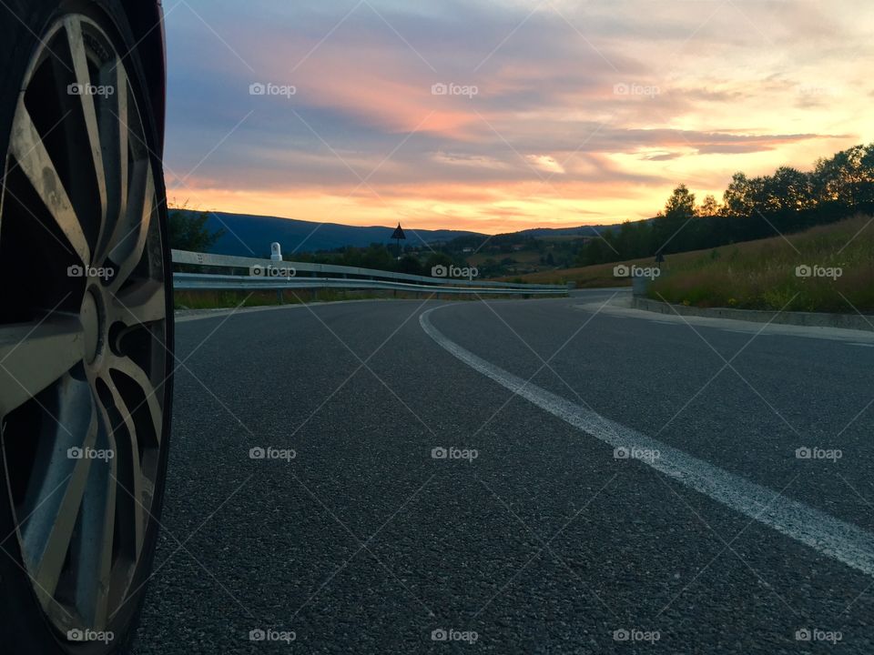 Focus on car wheel on the road with sunset ahead