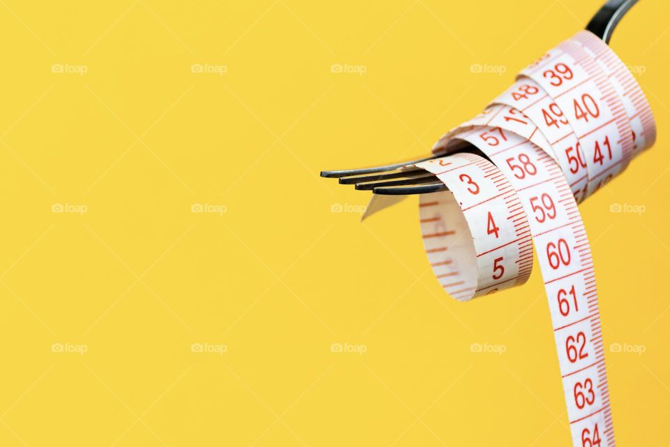 Fork and measuring tape on yellow background 