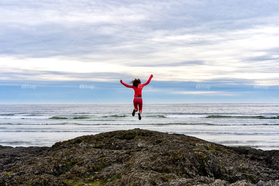 Girl jumping into the vast blue ocean from a rocky outcropping 