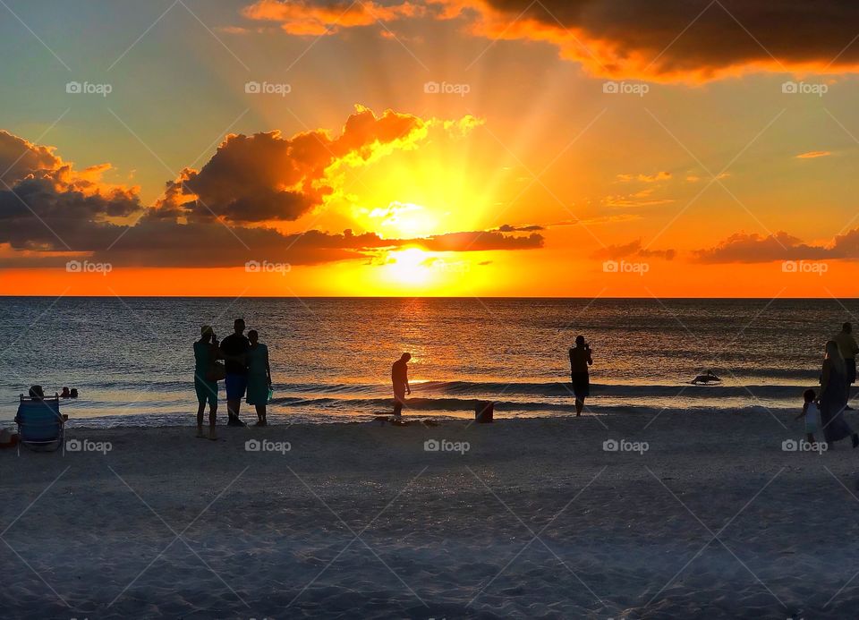 A road trip to a gorgeous fiery beach sunset with people bathing in the light.