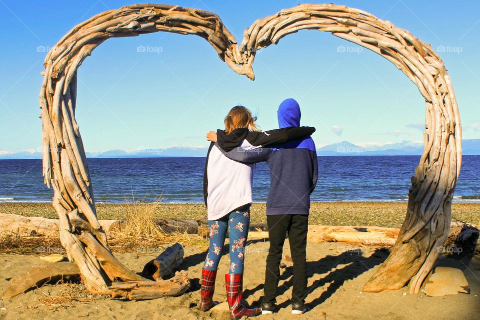 What’s that driftwood heart doing on the beach?? Two young friends pose under the heart on our local beach. A favourite spot for wedding photos!