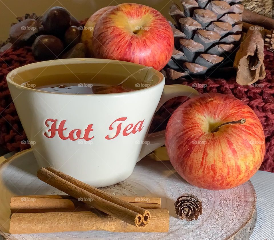 Hot apple & cinnamon tea on wood platter, with fruit, spices and pine cones