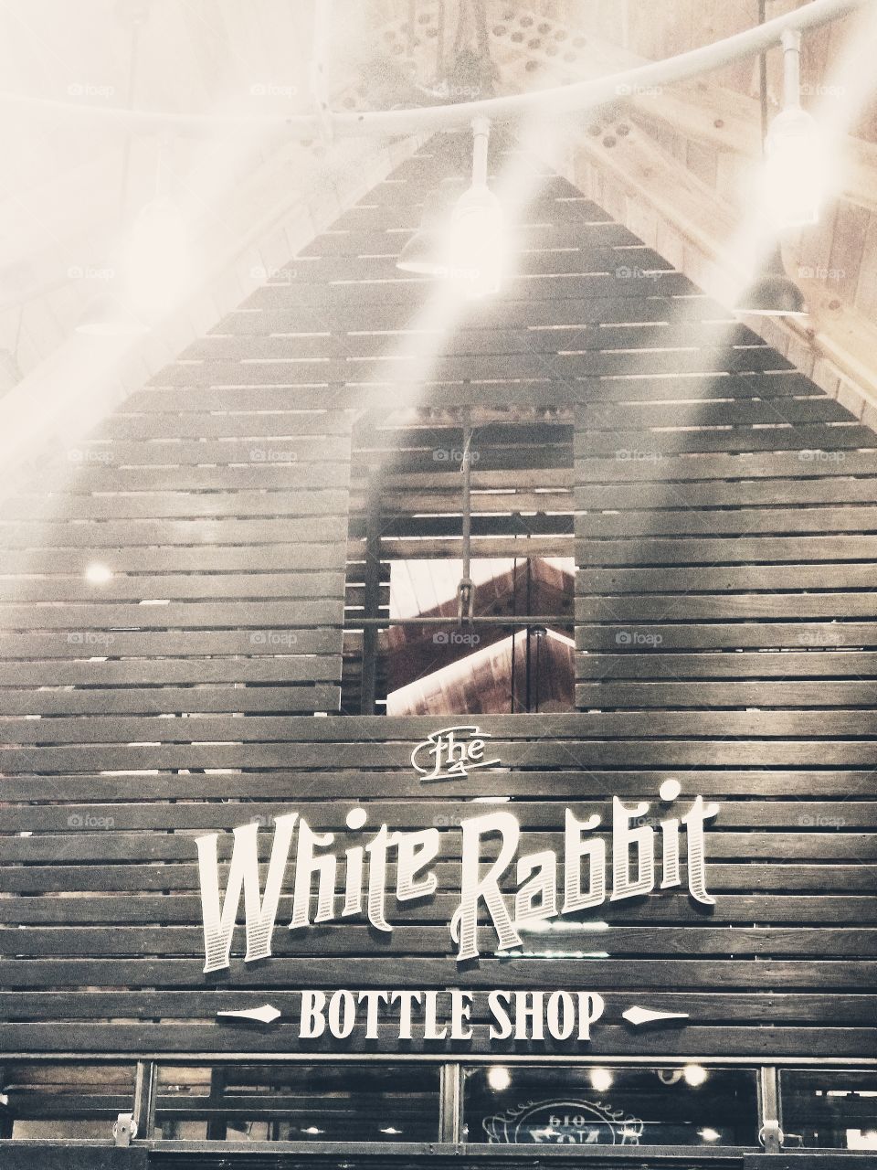 Vintage look entrance with weathered black barn wood panels, white lettering, & soft glow lights at the White Rabbit Bottleshop at Jack Daniel's distillery.