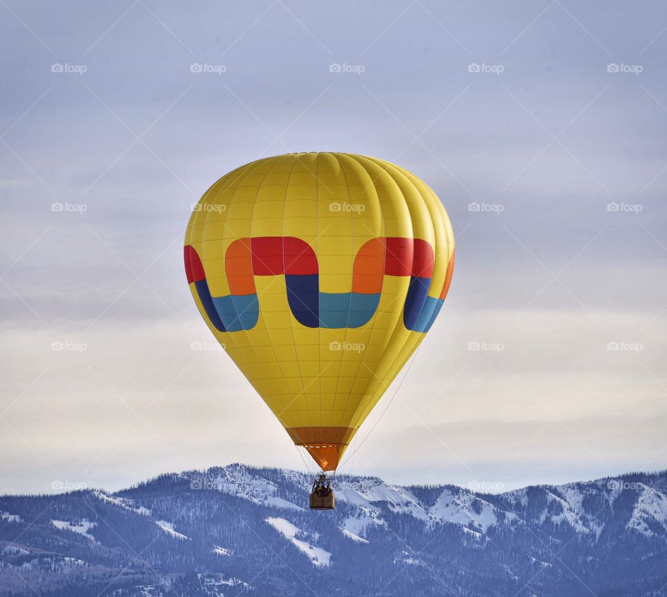 A hot air balloon festival in the winter creates a colorful scene. Mountains set a surreal background.