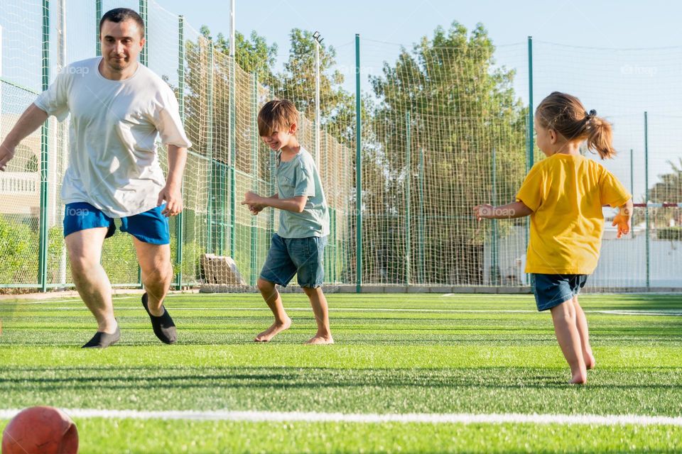 Full body man playing football with children on green lawn. Father's Day concept.