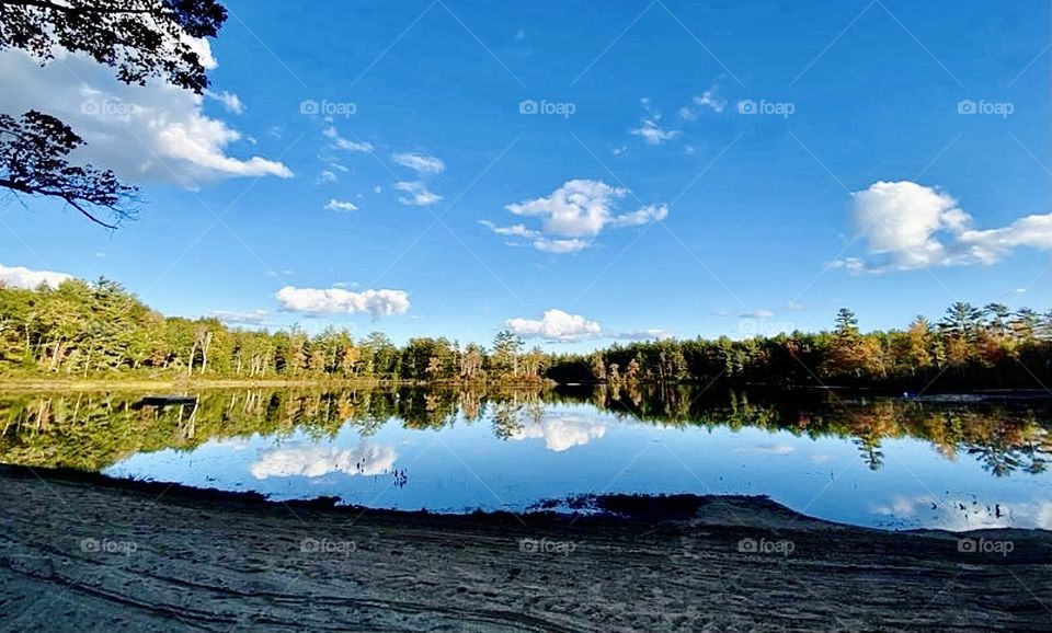 Standing by a lake in Shir-Roy New Hampshire on a picturesque day staring at the puffy clouds against the blue sky and scenic reflections in the water 