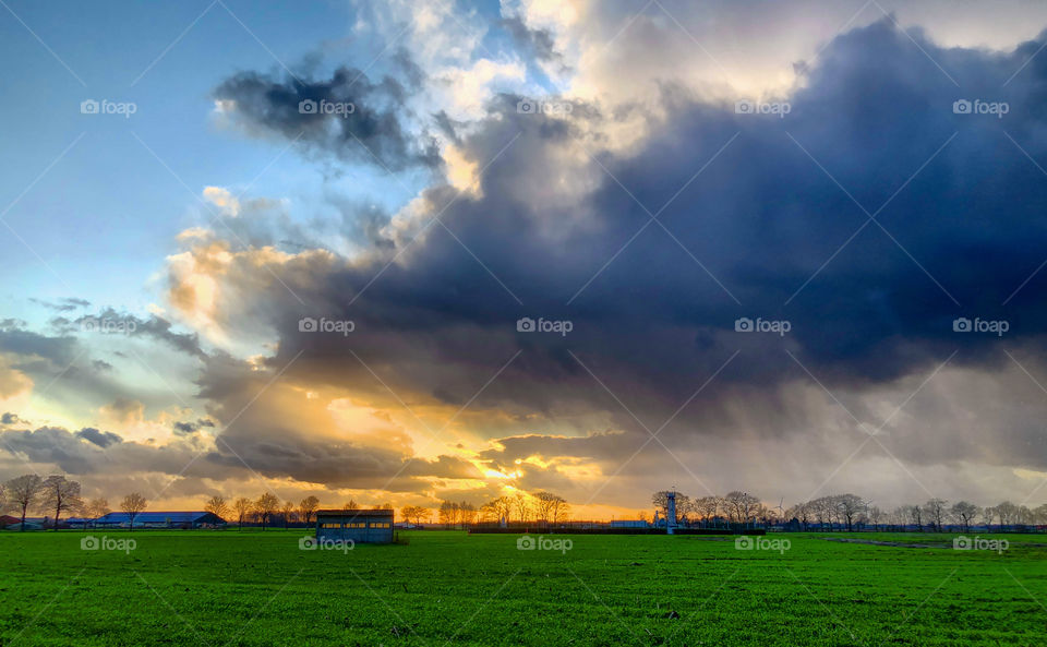 A dark an treathening Storm arises over a sunset farmfield landscape