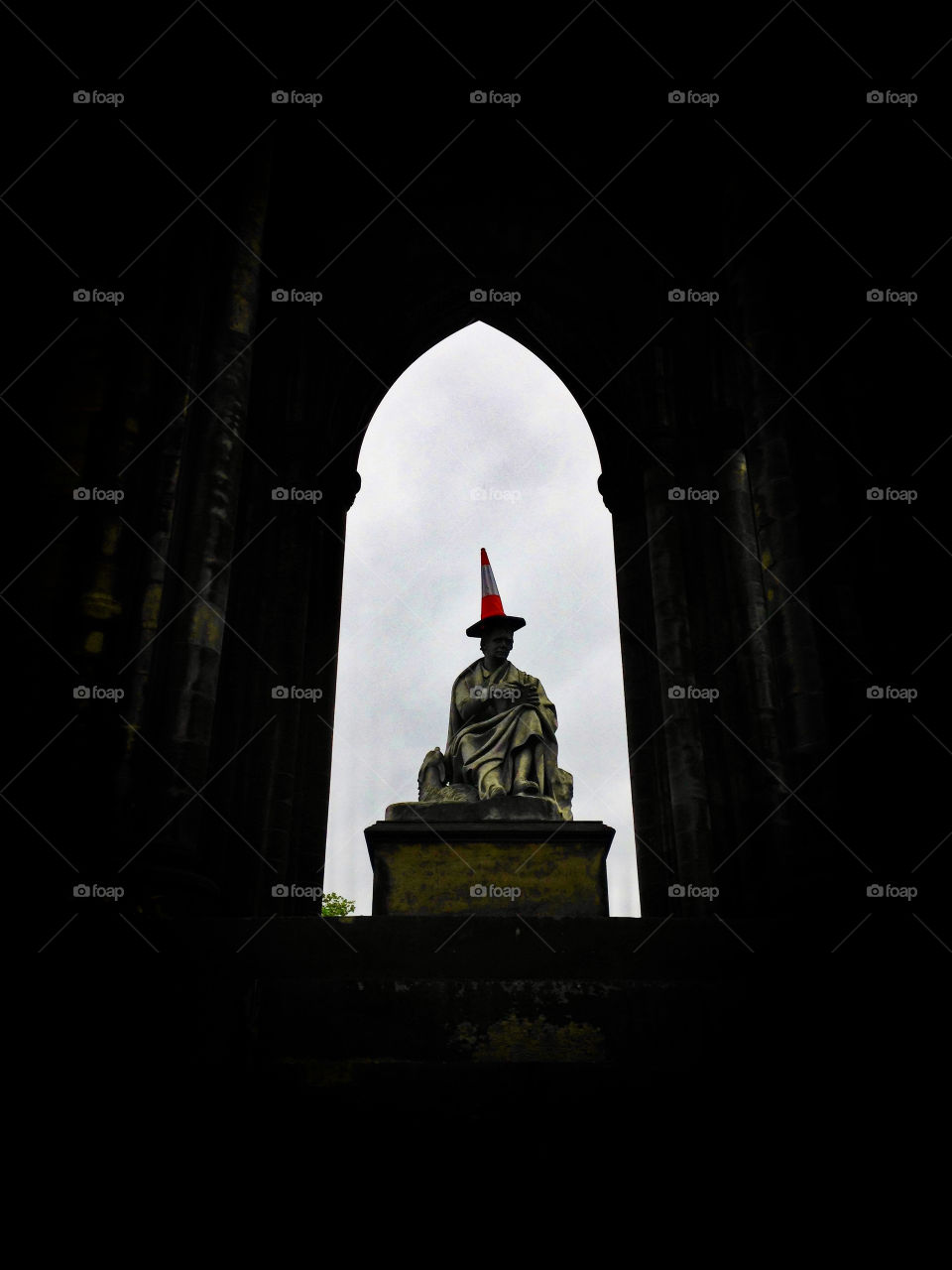 The iconic Scott Monument in Edinburgh, Scotland, with a traffic cone on the statue’s head. Statue of Sir Walter Scott against a cloudy sky. An iconic landmark and tourist destination in the Scottish city.