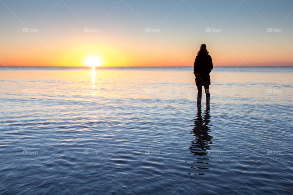 Silhouette standing in water at beach at sunrise sunset blue golden hour