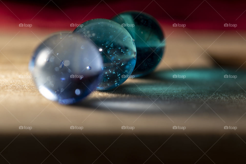 A portrait of three blue colored marbles shining their colorful light on to a wooden surface. they are different shades of blue.