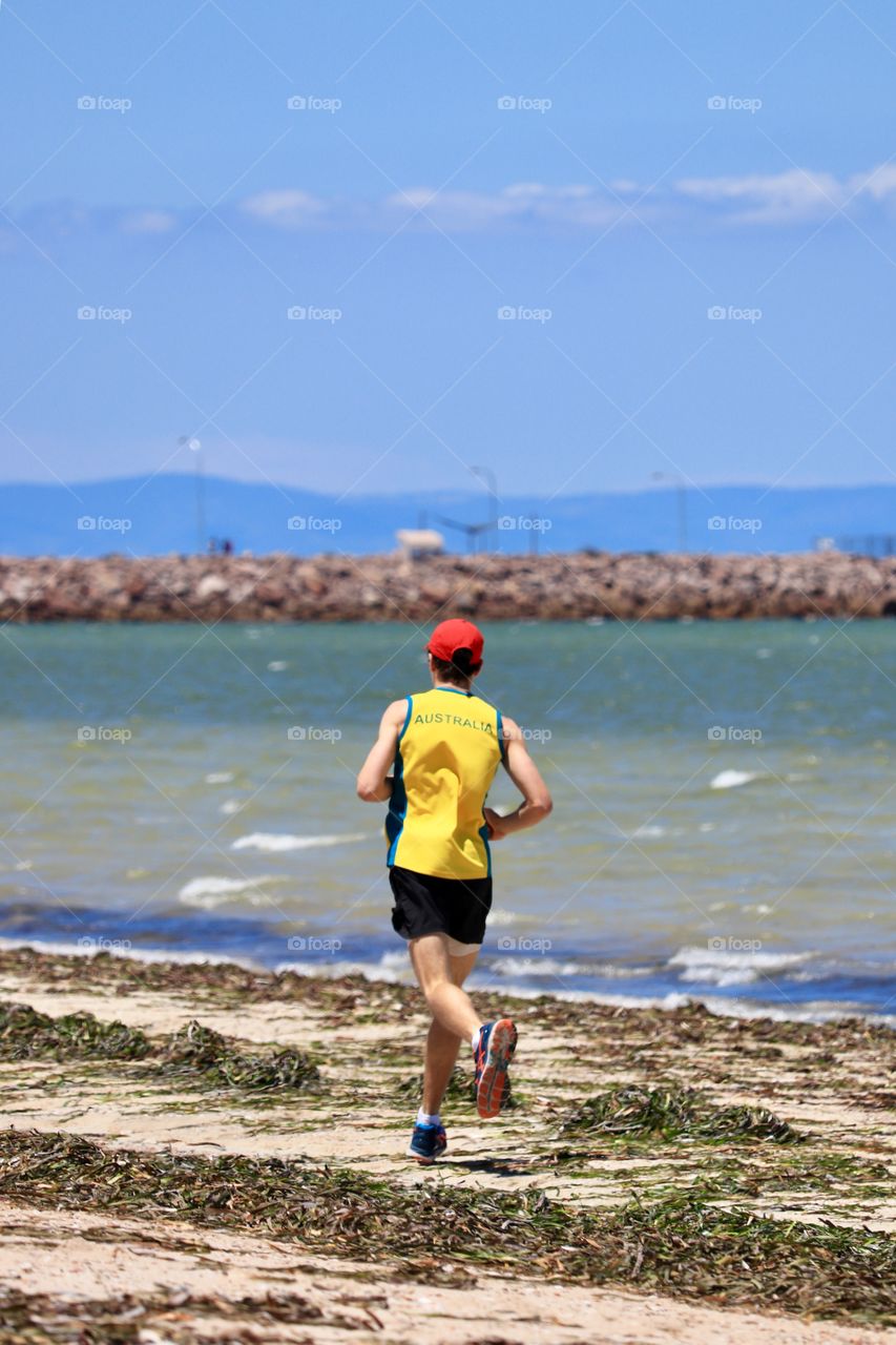 Male jogger wearing athletic “Australia” shirt on beach near marina 