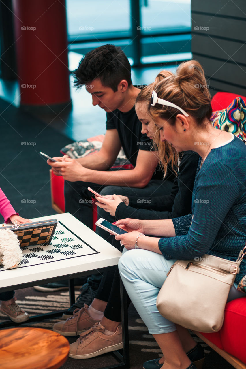 Family members using mobile phones together, sitting on sofa in lounge in hotel