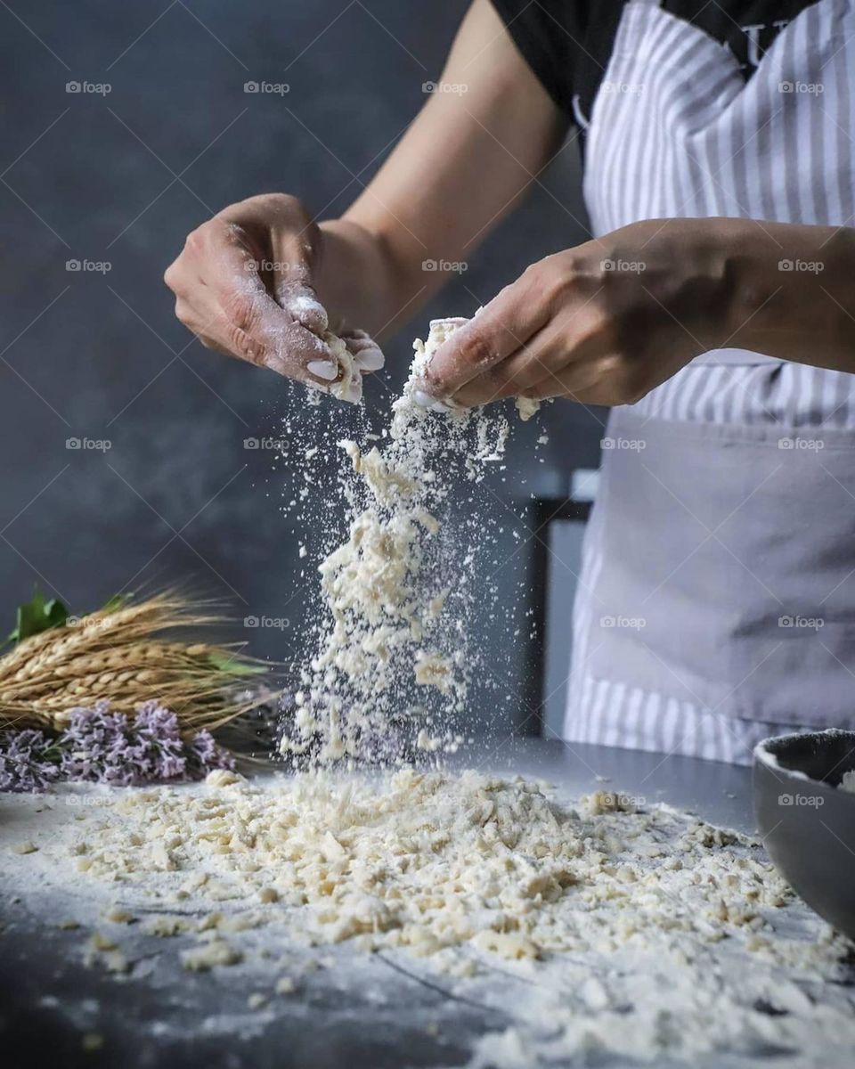 Prepares dough from flour for a future pie on a plain table and a background behind grains and flowers