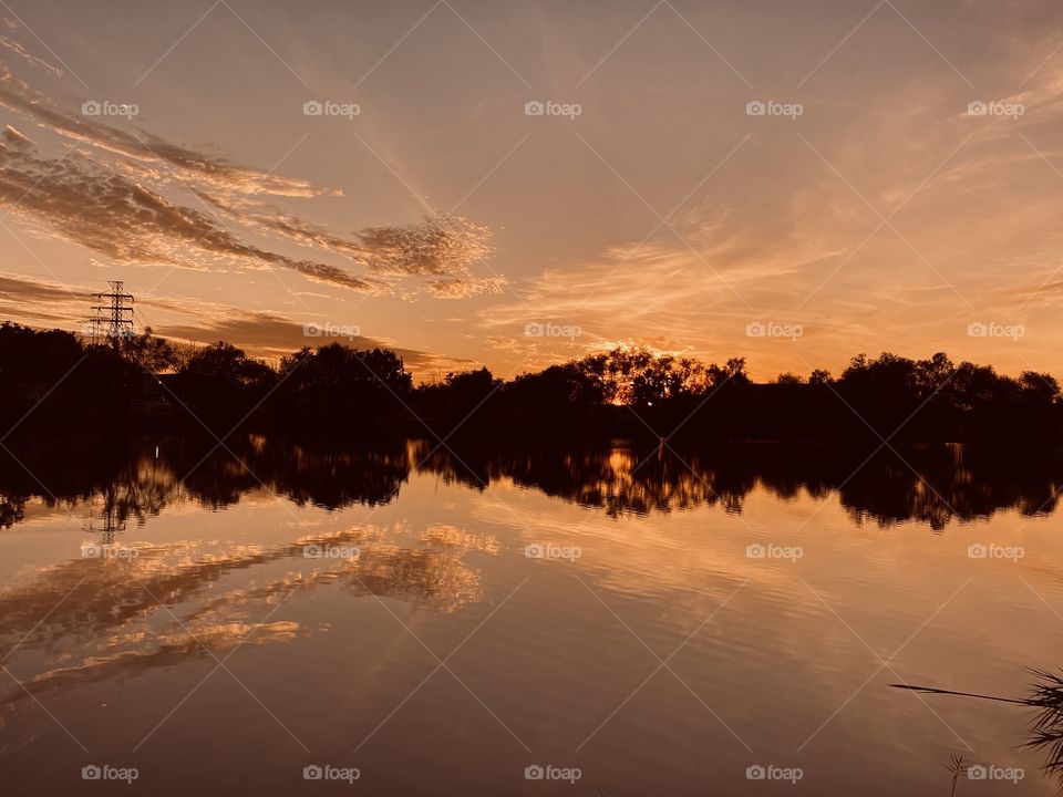 Sundown with high clouds grouping around the setting Sun. Reflectional Mirroring on top of lake water soaking up the colours for the sunset giving off bright Hues of interest.