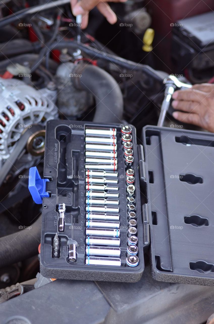 A man is working hard with car repairs to  his engine with a variety of tools as he attempts to install an alternator.