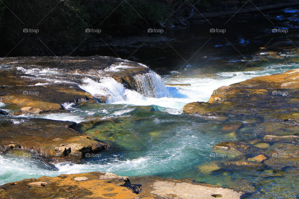 A blue-green, glacier-fed river tumbles and cascades over the smooth, brow, rocks creating pools, rapids and little waterfalls. The afternoon Spring sun made the water shine and sparkle as it followed its path downstream. 