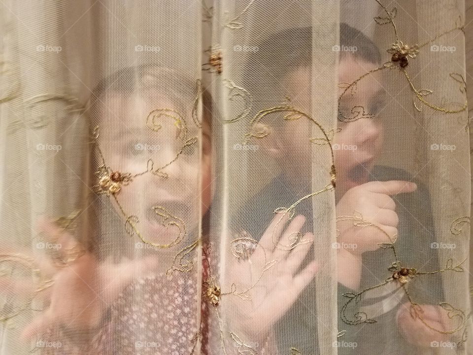 Brother and sister peeking behind the curtain