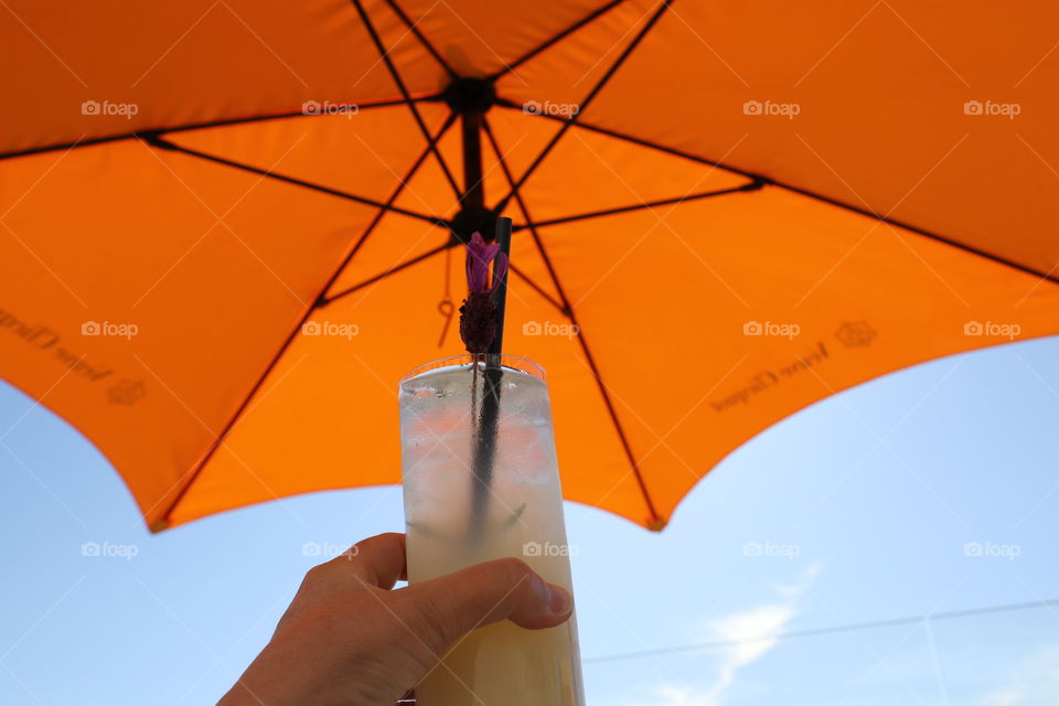 Refreshing drink under orange umbrella against clear blue sky