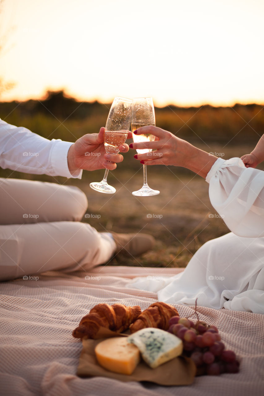 Romantic picnic for two on a sunset background. Two pieces of cheese, grapes, two croissants and two empty glasses lie on a blanket