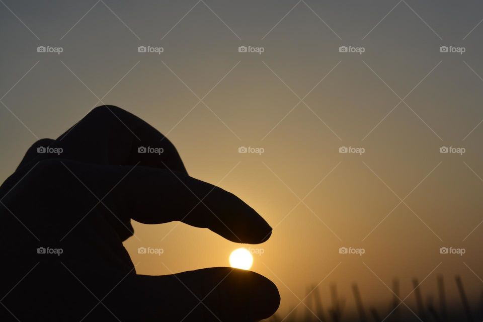 hand holding the sun at sunset