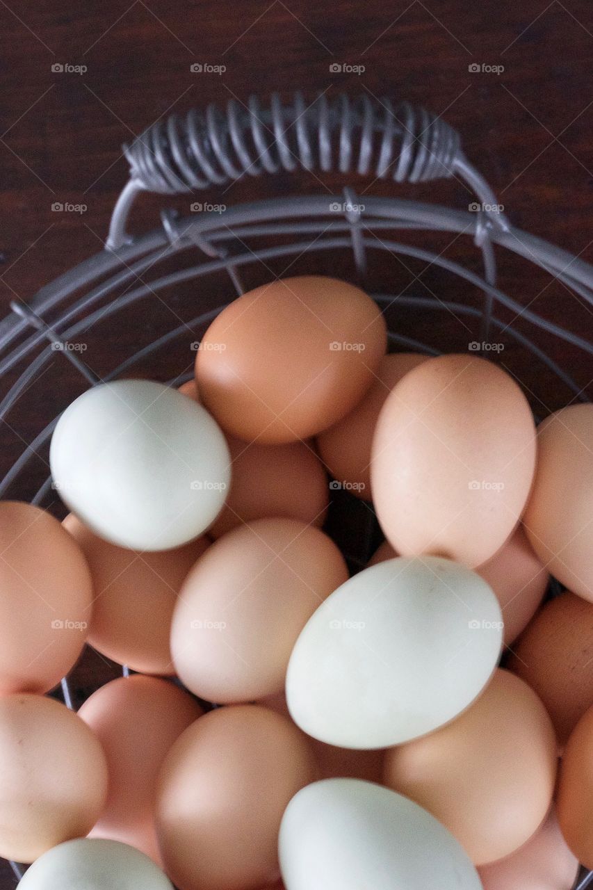 Overhead view of farm-fresh blue and brown eggs in a wire basket on a dark wooden surface