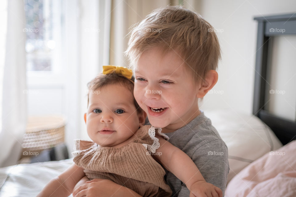 Smiling toddler boy hugging his little baby sister