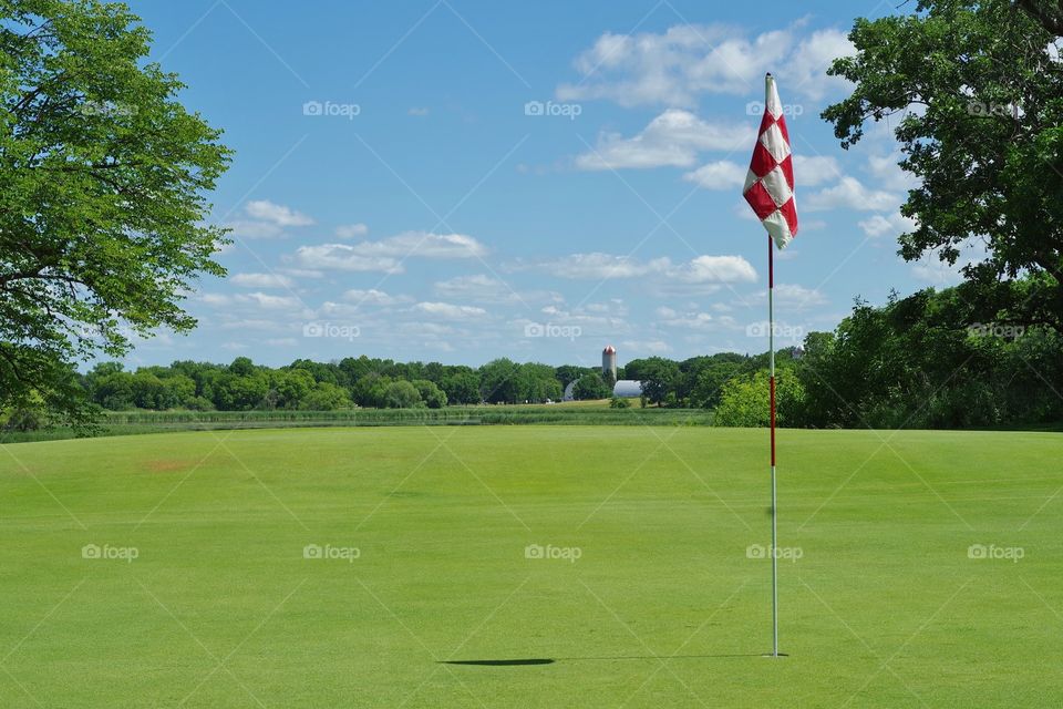scenic view from the green with the flag pole on a golf course with a farm in the background