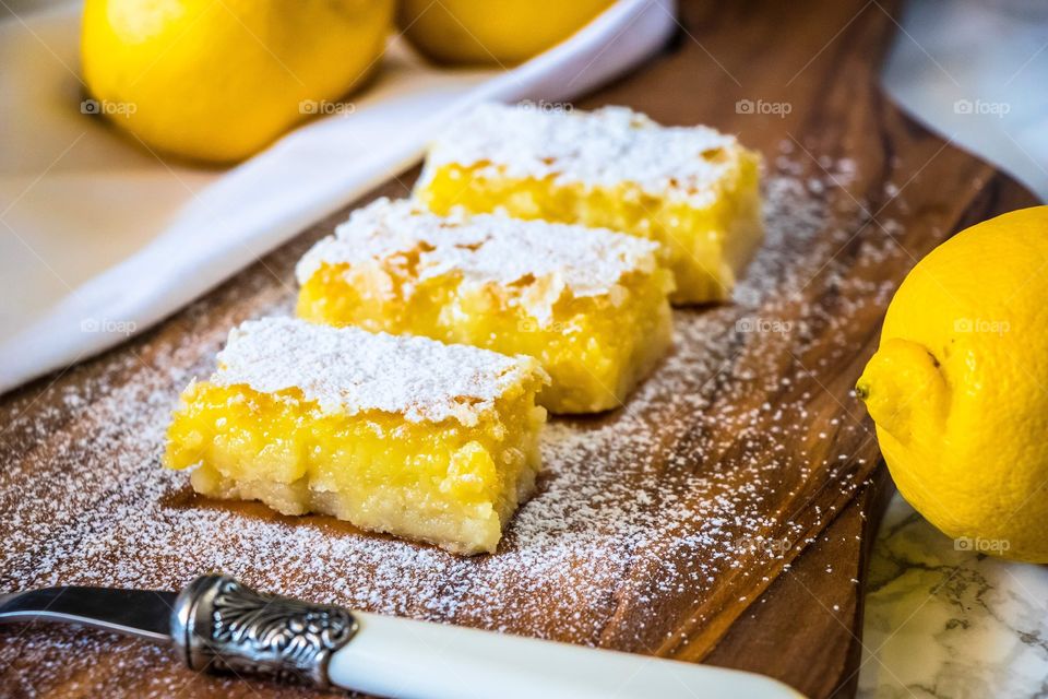 Lemon curd bars covered with icing sugar, served on a chopping board with lemons in the background